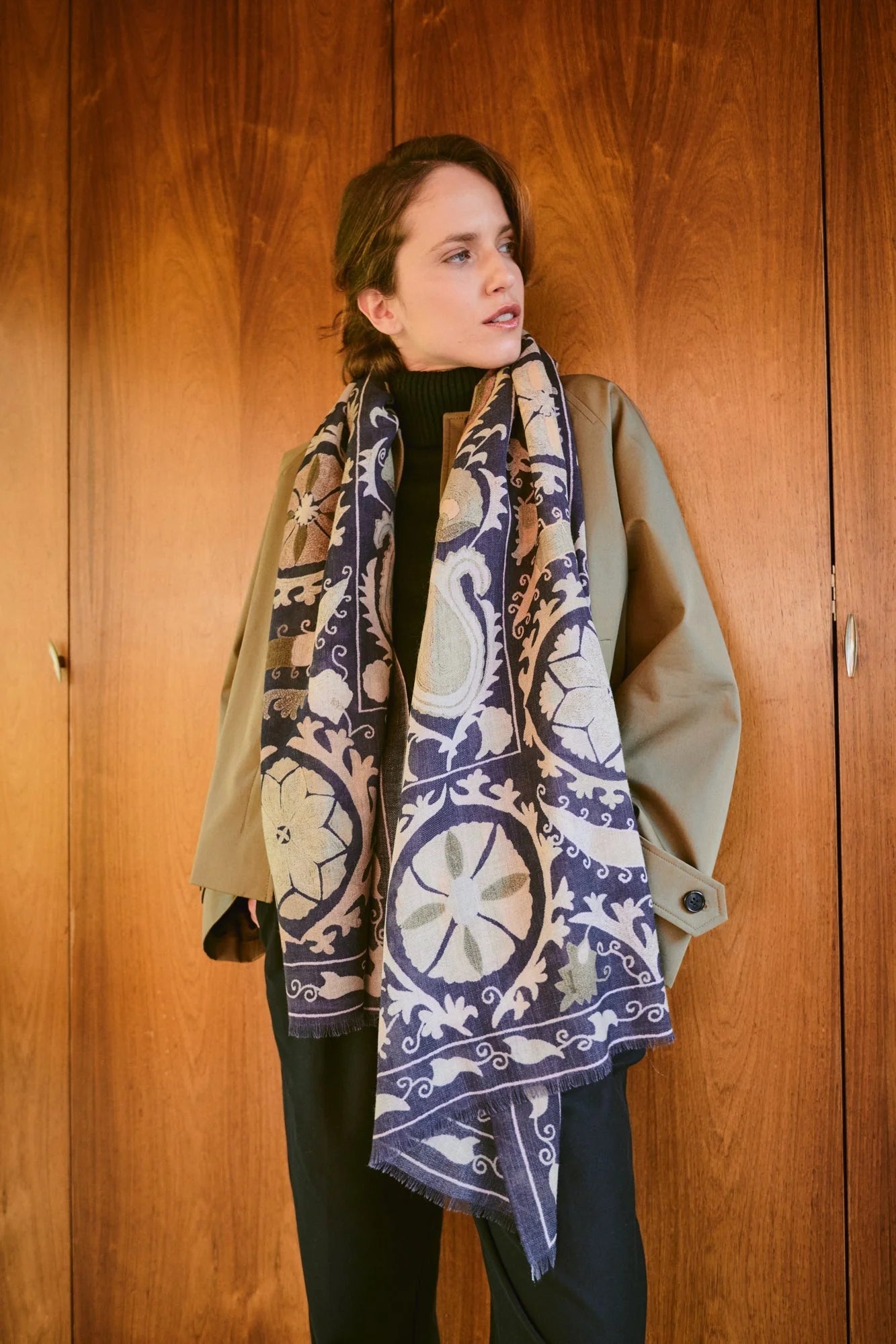Woman wearing One Hundred Stars Wool Scarf wth a grey background and a susani print in lighter colour.