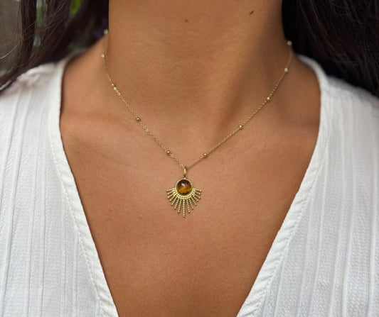 Gold necklace with a sun-shaped pendant worn by a person in a white top.