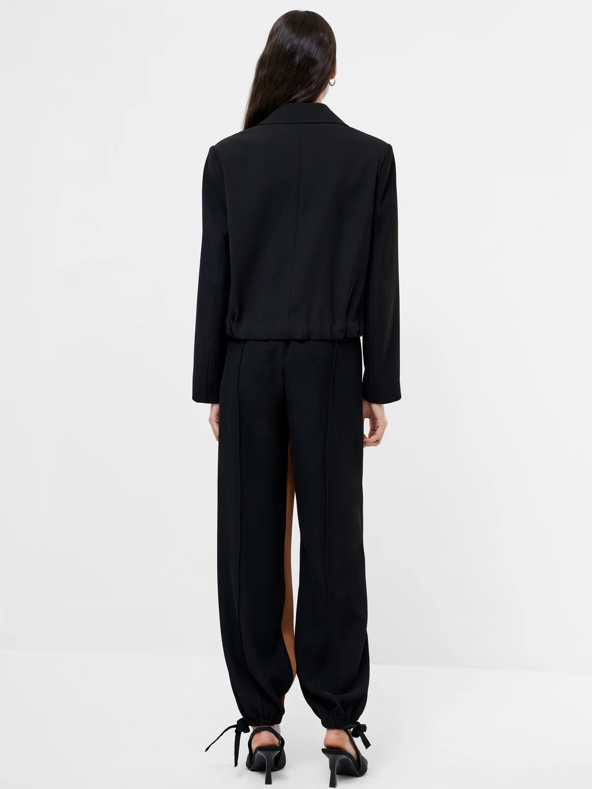 Women wearing a black cropped suit jacket with collar, 4 double breasted buttons and ruched bottom to jacket.  Back View