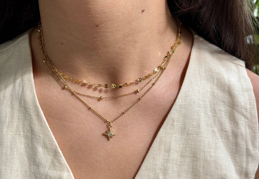 Close-up of a person wearing a triple layered gold necklace with a star pendant.