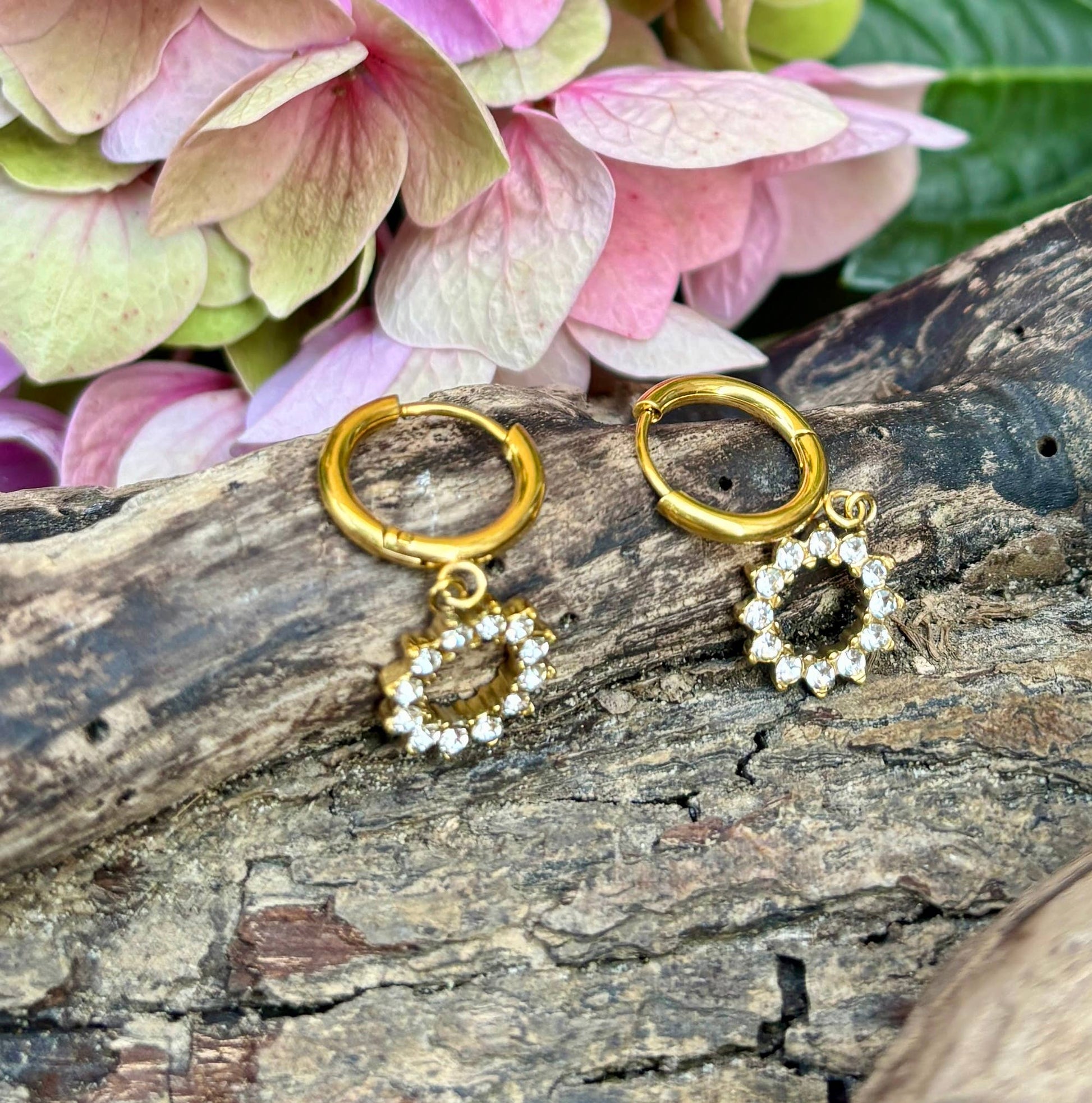 Gold hoop earrings with star-shaped charms on a wooden surface with flowers in the background