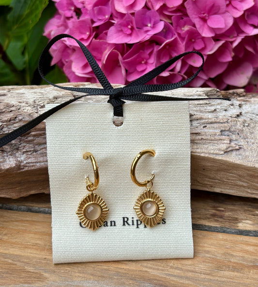 Gold hoop earrings on a branded card with pink flowers in the background