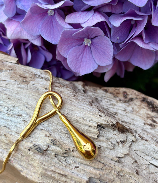 Gold necklace with a pendant on a wooden surface with purple flowers in the background
