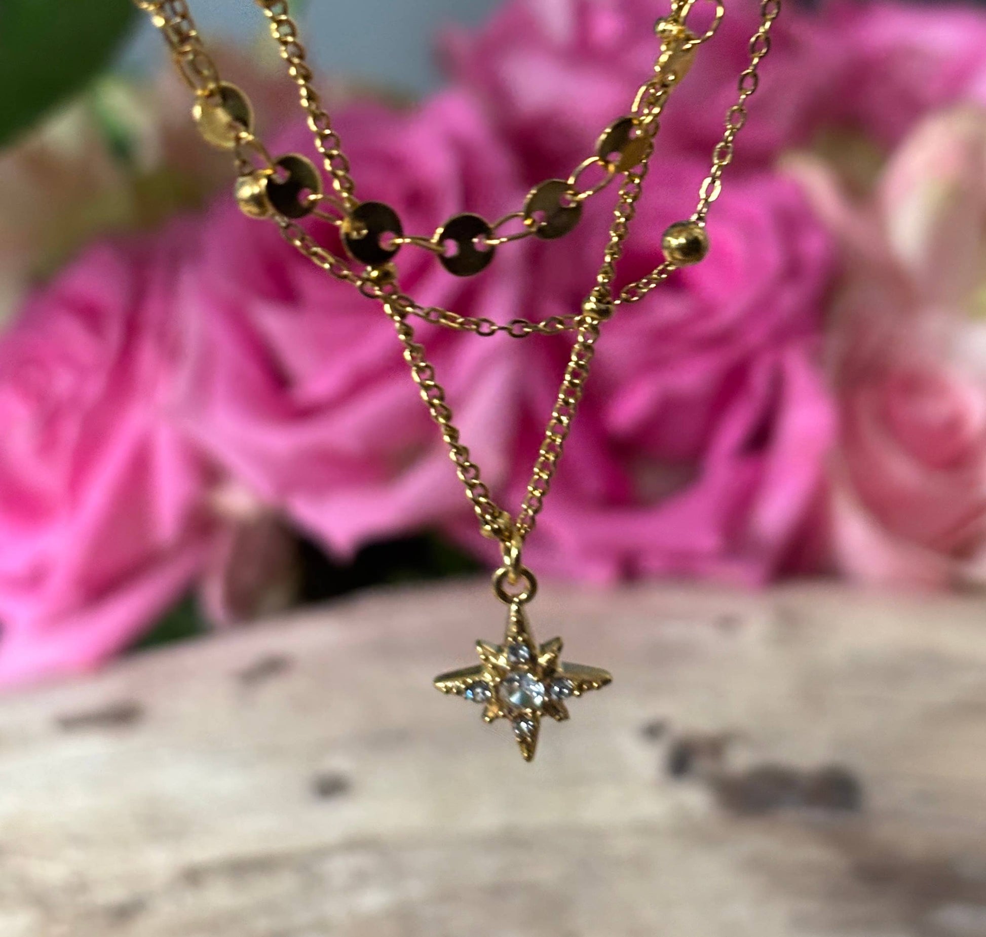 Gold necklace with a star pendant in front of pink flowers