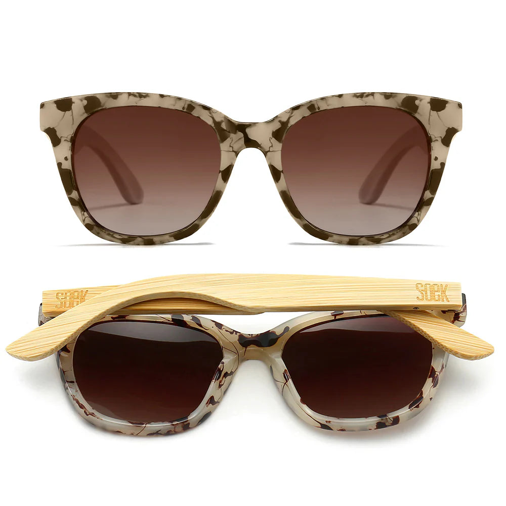 Sunglasses with tortoiseshell frame and brown gradient lenses, accompanied by a wooden arm on a white background.