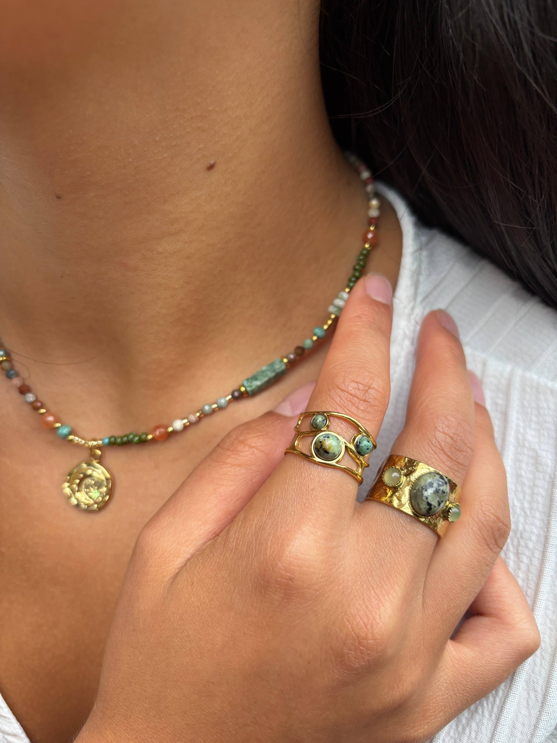 Close-up of a person wearing a beaded necklace and two gold rings with gemstones.
