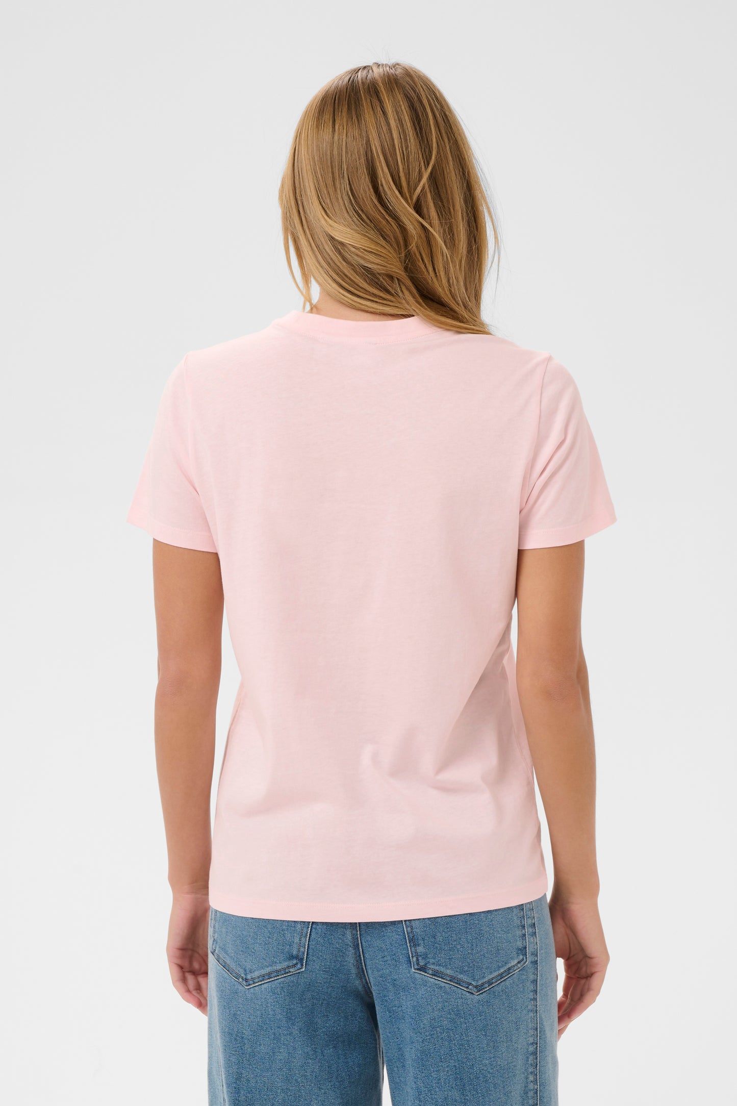 Woman wearing a pink t-shirt with text and blue jeans on a white background
