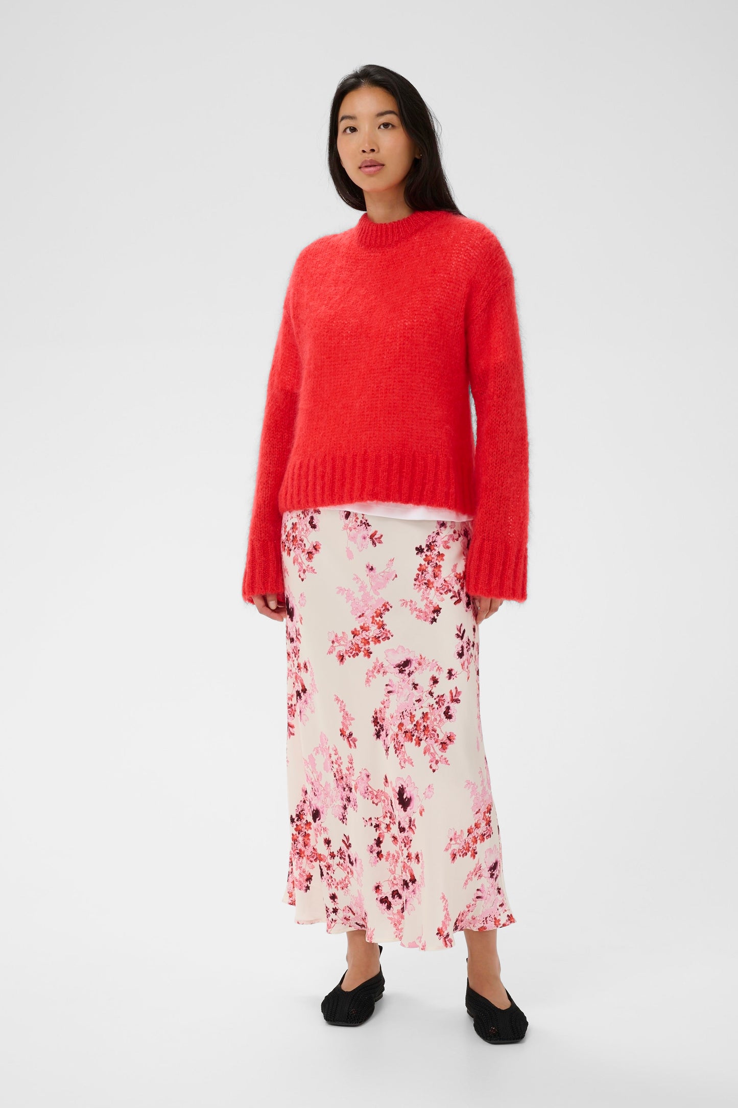Woman wearing a red sweater and floral skirt on a white background
