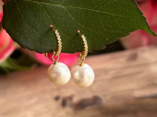 Pearl earrings with gold hooks on a green leaf